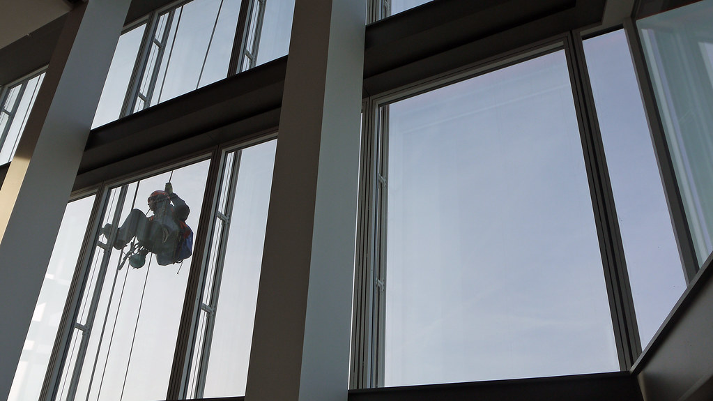 Rope-access window cleaner silhouetted while working down a tall glass atrium