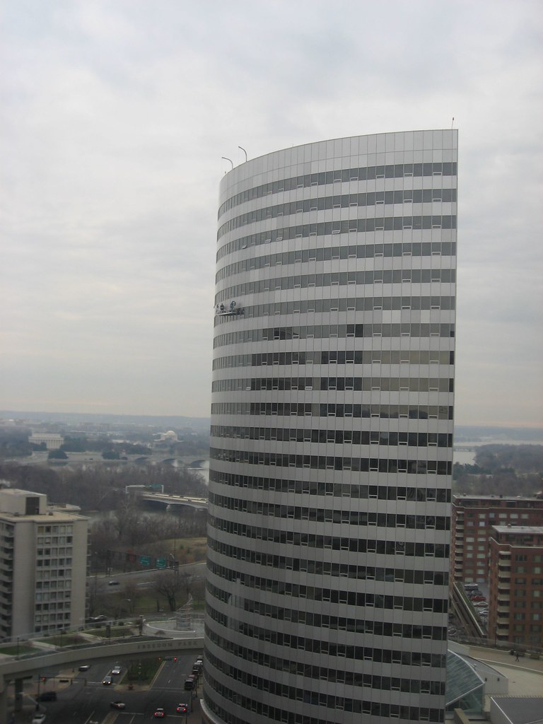 Curved glass office tower with two tiny window washers on a suspended platform halfway up the facade